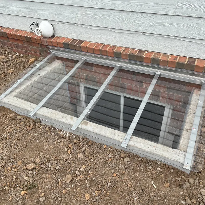 Window well cover closed, top-down view showing aluminum frame and clear polycarbonate